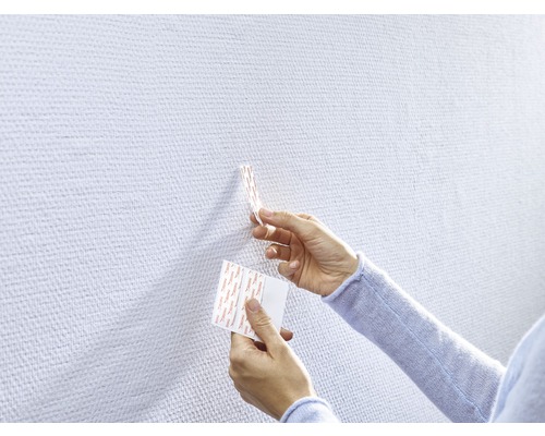 Person befestigt Klebestreifen an einer Wand