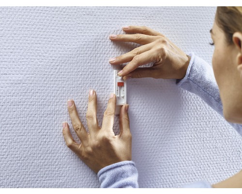 Frau befestigt einen Klebehaken an der Wand