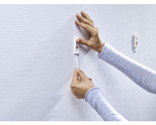 Person befestigt einen Klebehaken an einer Wand.