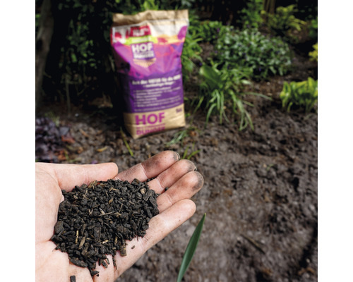 Hand hält Bodenverbesserer vor einem Sack Hof-Bodenverbesserer im Garten.