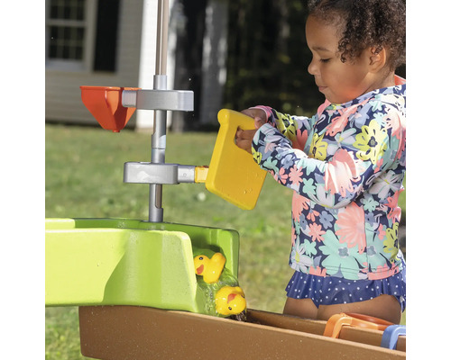 Mädchen spielt mit einem Wasserspieltisch mit gelben Enten und Eimer im Garten