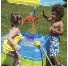 Zwei Kinder spielen an einem blauen und grünen Wasserpieltisch mit Sonnenschirm im Garten.