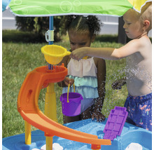 Kinder spielen mit einem Wasser-Spieltisch mit Sonnenschirm im Garten