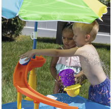 Szene mit Kindern, die mit einem Wasserspieltisch mit Sonnenschirm im Freien spielen.