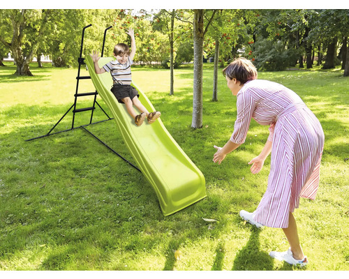 Junge rutscht auf einer Gartenrutsche, während eine Frau ihn auffängt