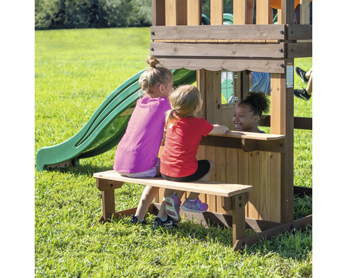 Drei Kinder spielen auf einem Holzspielplatz mit Rutsche und Sitzbank