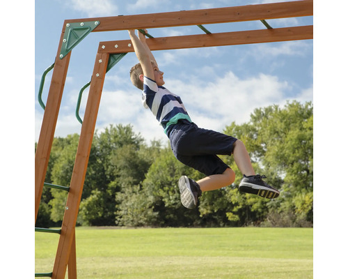 Junge hangelt sich an einer Kinderschaukel im Garten entlang.