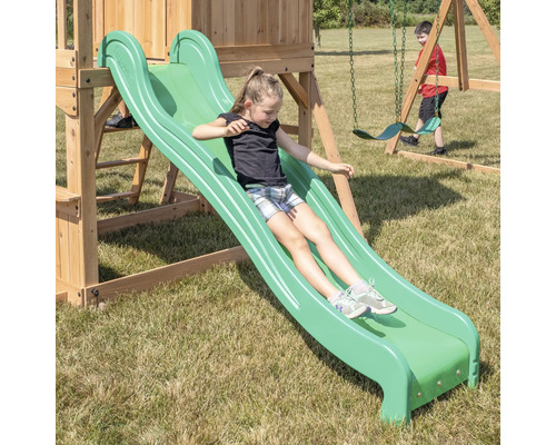 Mädchen rutscht auf einer grünen Rutsche eines Holzspielturms