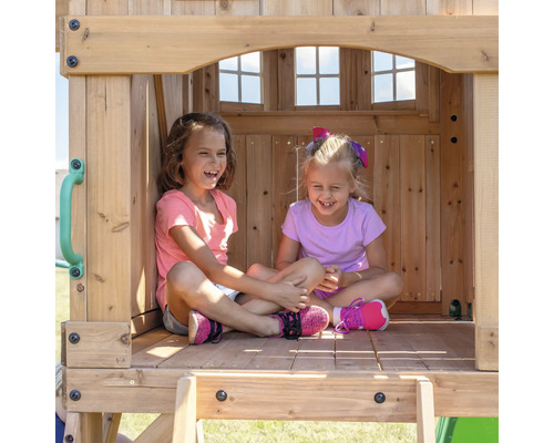 Zwei lachende Mädchen sitzen in einem Spielhaus aus Holz.