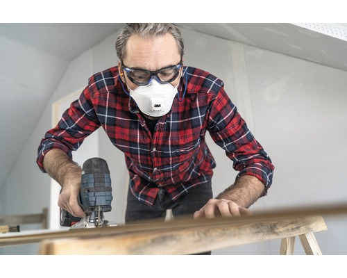 Mann arbeitet mit einer Stichsäge, trägt dabei Schutzbrille und Staubmaske.