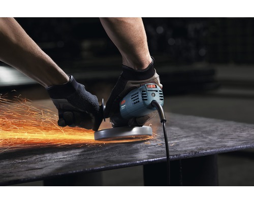 Ein Mann bearbeitet mit einem Winkelschleifer ein Metallstück, wodurch Funken entstehen.