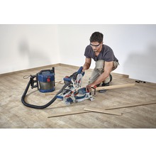 Mann arbeitet mit einer Kappsäge und einem Staubsauger auf einem Holzboden.