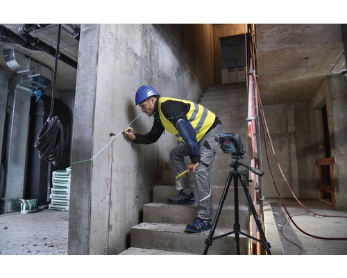 Ein Bauarbeiter arbeitet mit einem Linienlaser auf einer Baustelle, um eine gerade Linie an einer Betonwand zu markieren.