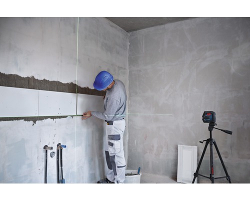 Ein Mann verlegt Fliesen mit einem Linienlaser in einem Raum.