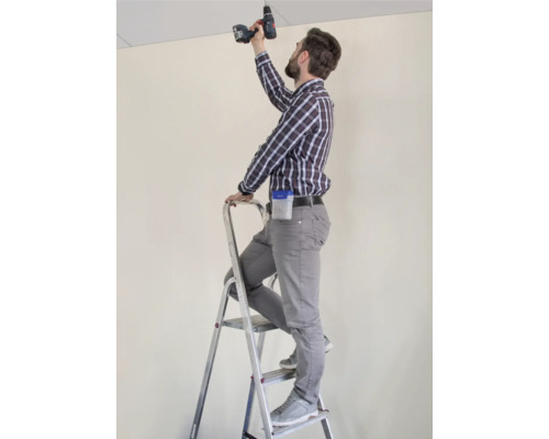 Handwerker auf einer Leiter, der mit einem Akkuschrauber an einer Decke arbeitet