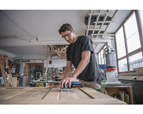 Mann schleift Holztür mit einem Multischleifer in einer Werkstatt