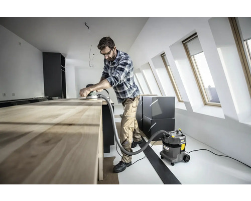 Handwerker schleift Holztisch mit Schleifgerät und Staubsauger in heller Dachgeschosswohnung.