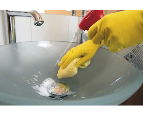 Reinigung eines Badezimmerwaschbeckens mit Reinigungsmittel und Handschuhen