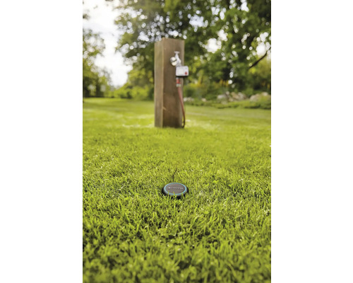 Szene mit einem Bewässerungssensor im Gras und einem Wasserhahn im Hintergrund.