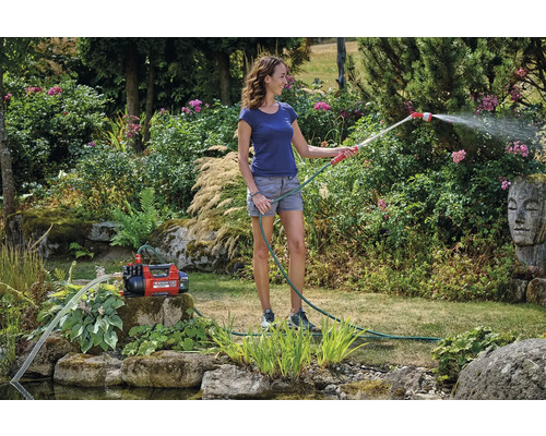 Frau bewässert Garten mit Gartenpumpe und Gartenschlauch