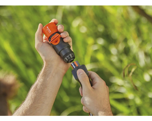 Eine Person verbindet ein Gardena Wasserstop-Anschlussstück mit einem Gartenschlauch.