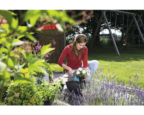 Eine Frau bepflanzt im Garten einen Blumentopf.