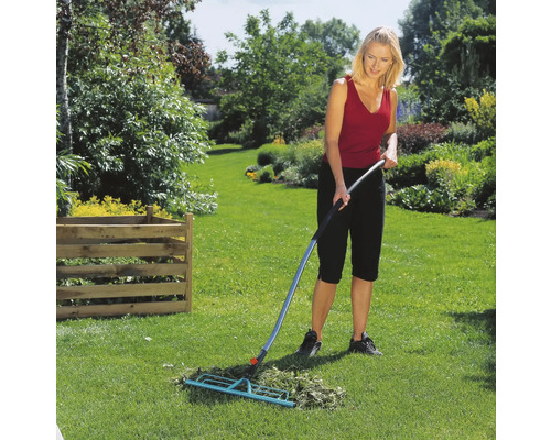 Frau harkt Gras mit einem Fächerbesen im Garten