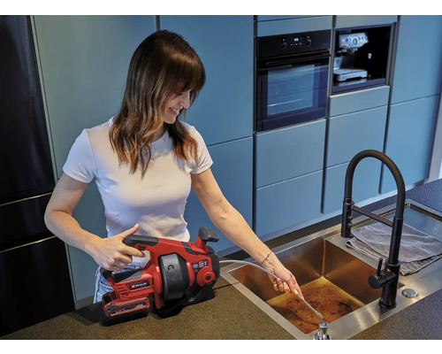 Frau benutzt eine Rohrreinigungsspirale von Einhell, um ein Abflussrohr zu reinigen.