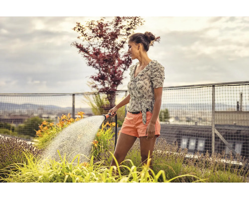 Frau gießt Pflanzen auf einem Dachgarten mit einem Gartenschlauch