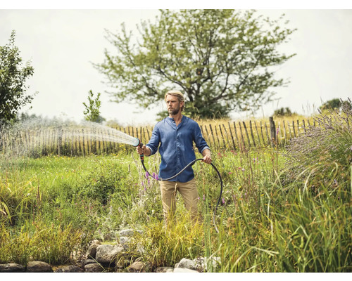 Mann bewässert Garten mit Gartenschlauch und Spritzpistole