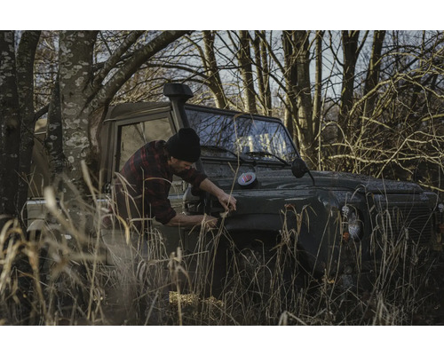 Mann befestigt etwas an einem Geländewagen im Gelände