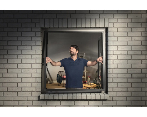 Mann öffnet ein Fenster mit Kippfunktion in einem Backsteinhaus.