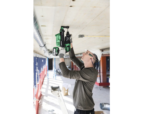 Ein Mann bohrt mit einem Akku-Bohrhammer in eine Betondecke auf einer Baustelle.