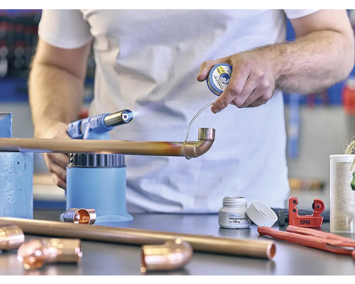 Ein Mann lötet ein Kupferrohr mit einem Lötbrenner und Lötzinn