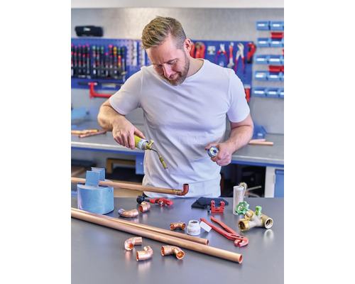 Ein Mann lötet Kupferrohre mit einem Gasbrenner in einer Werkstatt.