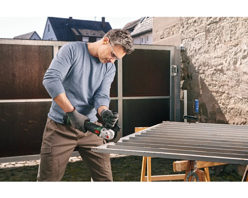 Mann schleift Metalltor mit einem Winkelschleifer im Freien.