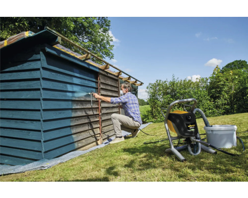 Mann streicht Holzschuppen mit Farbsprühsystem