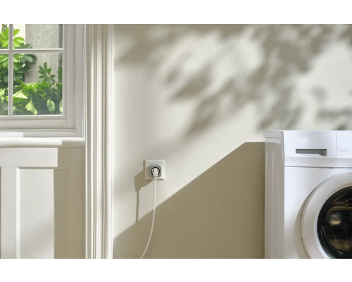 Intelligente Steckdose mit Waschmaschine im Hintergrund.