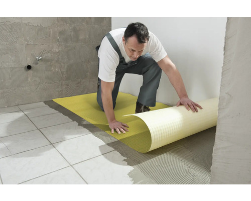 Ein Mann verlegt eine Entkopplungsmatte auf einem gefliesten Boden.