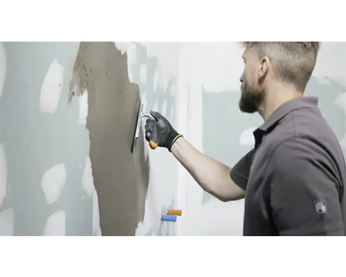 Mann spachtelt Wand mit Spachtelmasse