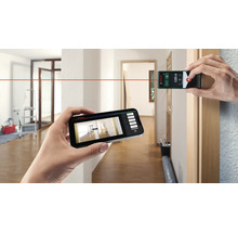 Person misst einen Raum mit einem Laserentfernungsmesser und einem Smartphone. Bosch Logo.