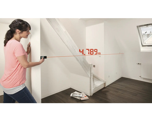 Frau misst mit einem Laser-Entfernungsmesser einen Raum mit Treppe.