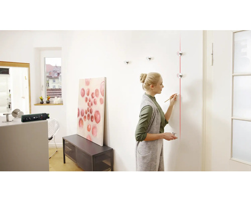 Frau richtet mit einem Linienlaser eine Garderobe an einer Wand aus