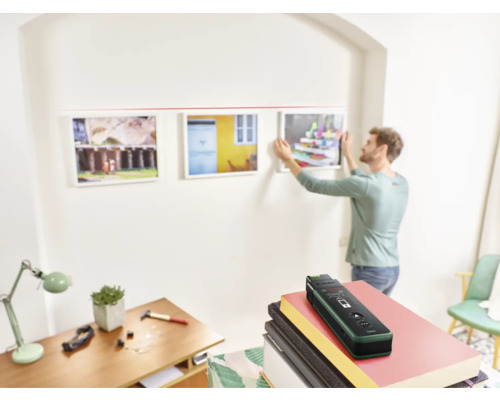 Mann hängt mit einem Ortungsgerät Bilder an einer Wand auf.