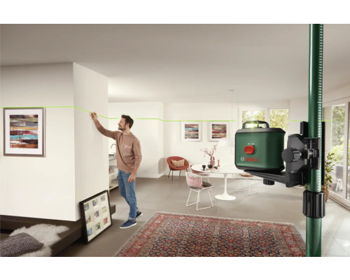 Raumszene mit einem Mann, der eine grüne Laserlinie mit einem Kreuzlinienlaser an einer Wand markiert