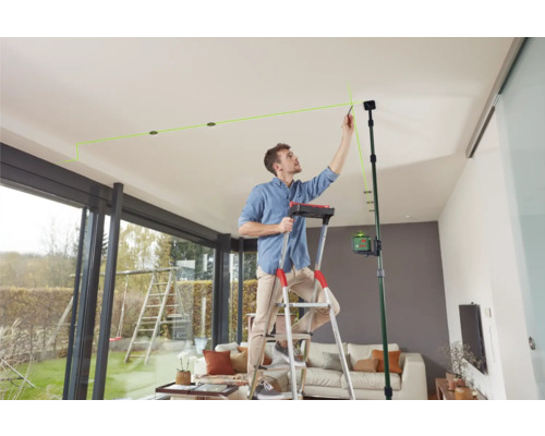 Mann auf einer Leiter, der mit einem Linienlaser Markierungen an der Decke anbringt.