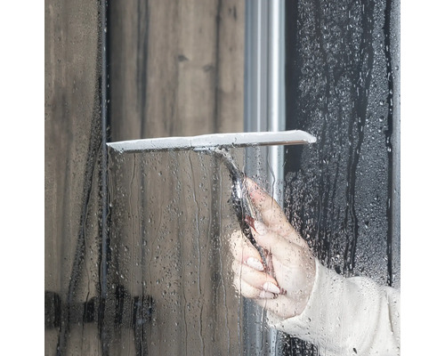 Eine Person benutzt einen Duschabzieher zur Reinigung einer Duschwand.