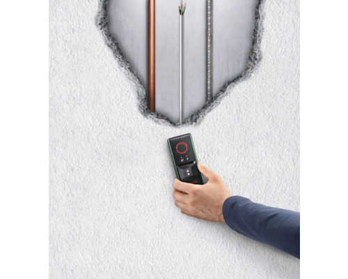 Hand hält ein Ortungsgerät vor einer Wand mit freigelegten Leitungen