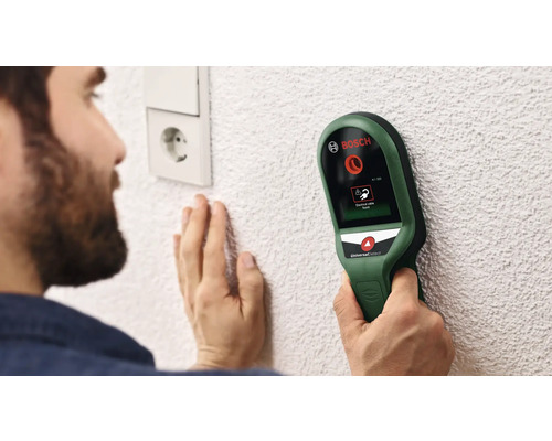 Eine Person benutzt ein Bosch UniversalDetect Ortungsgerät an einer Wand in der Nähe einer Steckdose, um elektrische Kabel zu finden.