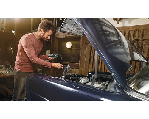 Mann prüft Autobatterie mit einem Batterietester in einer Garage